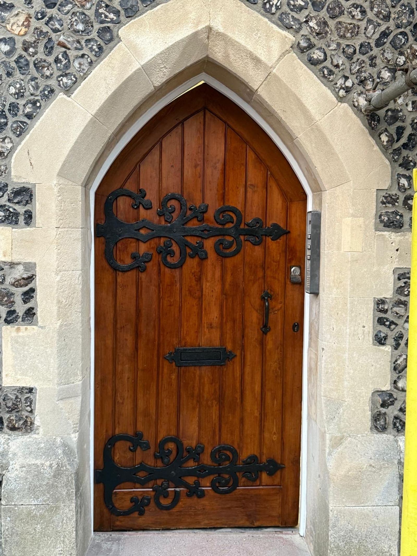 Restored arched oak front door with ornate black ironwork in a flint surround, Brighton